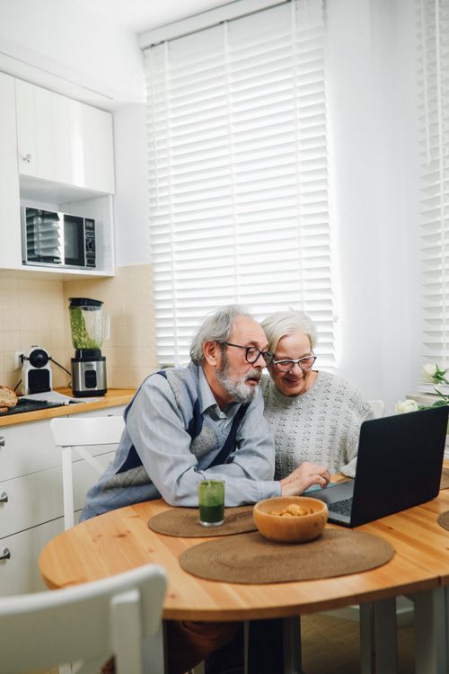 Free Elderly couple using a laptop in a bright kitchen, sharing moments of happiness and togetherness. Stock Photo