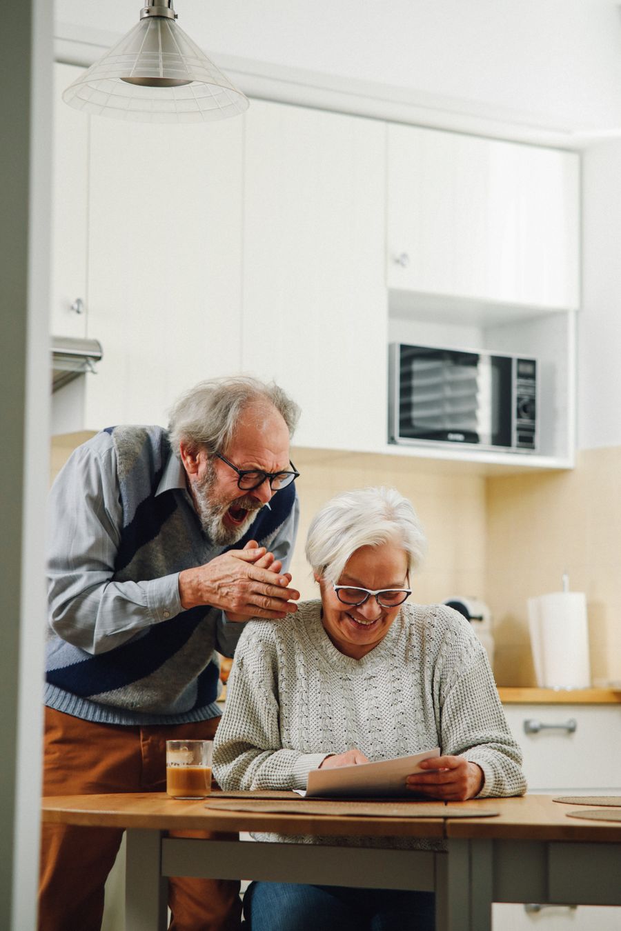 An older couple at their kitchen table, reading good news in a letter