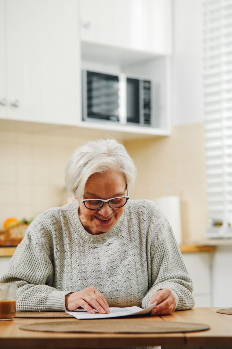 A woman smiling as she reads a letter at her kitchen table