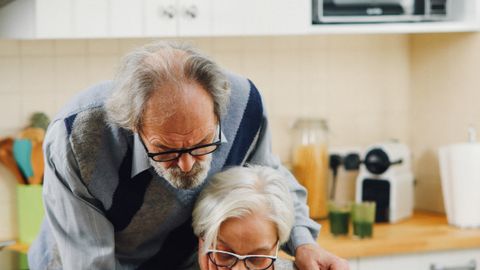 Elderly couple reviewing documents together at the kitchen table, focusing on financial plans.