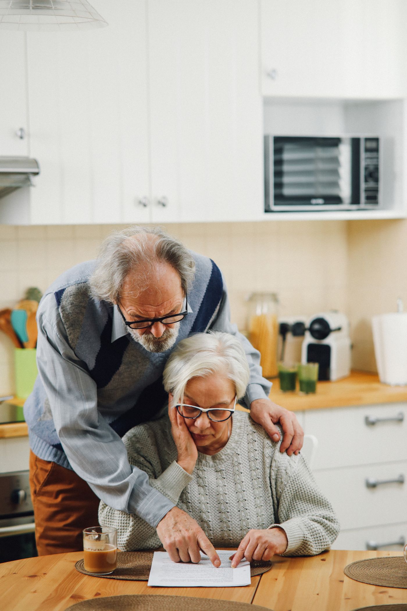 A woman reads a policy document at her kitchen table while her husband looks on.