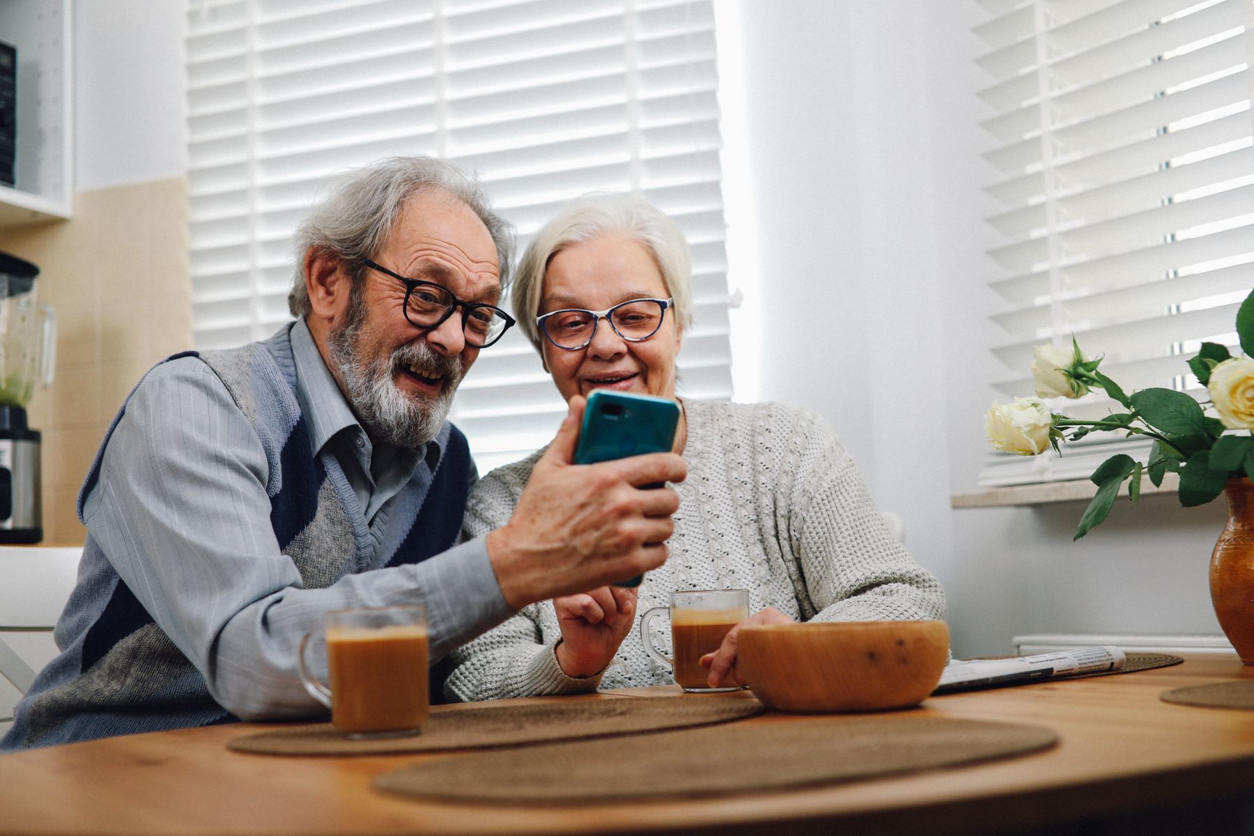 A couple at their kitchen table smiling while looking at a phone.