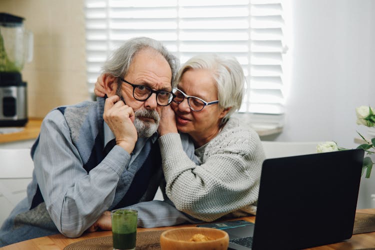 Elderly Couple Sitting At The Table Hugging And Using A Laptop 