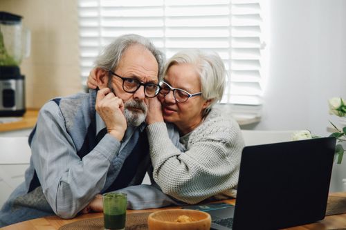 Free Senior couple affectionately using a laptop together at a table in their cozy home. Stock Photo