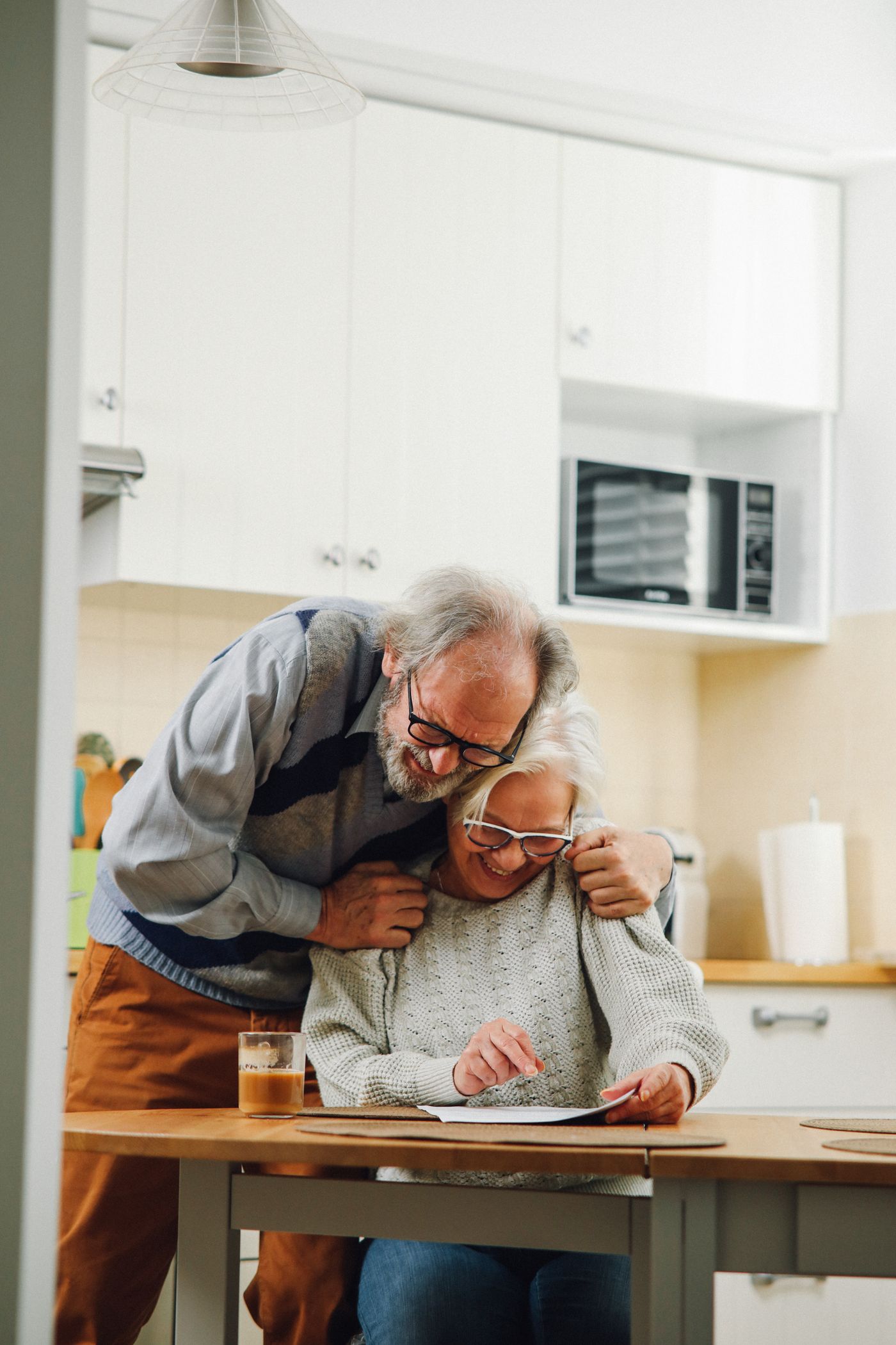 A couple share a hug at the kitchen table over their paperwork.