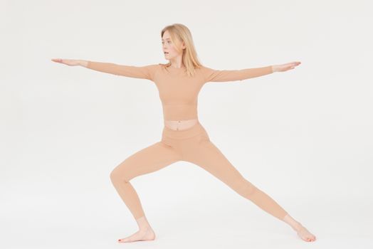Woman in warrior yoga pose wearing beige activewear. Promotes flexibility and healthy lifestyle.
