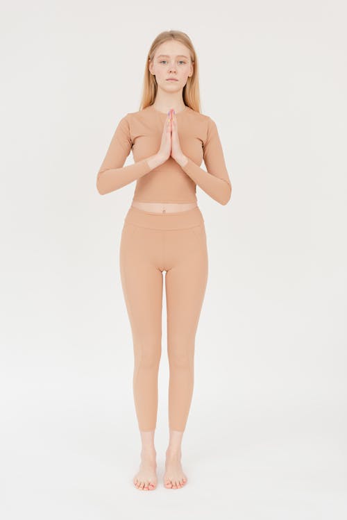 Free Full body of peaceful young barefooted female in trendy active wear standing in white studio in Tadasana pose with namaste hands and looking at camera during yoga session Stock Photo
