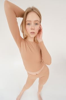 From above of self assured young fit female model in activewear touching long blond hair and looking at camera against white background