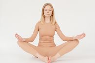 Full body of relaxed young female with blond hair in sportswear meditating with cosed eyes in Baddha Konasana pose while practicing yoga in white studio
