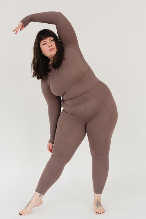 Free Full body of confident young overweight barefooted female with ling dark hair in sportswear bending aside and looking at camera while practicing yoga in white studio Stock Photo