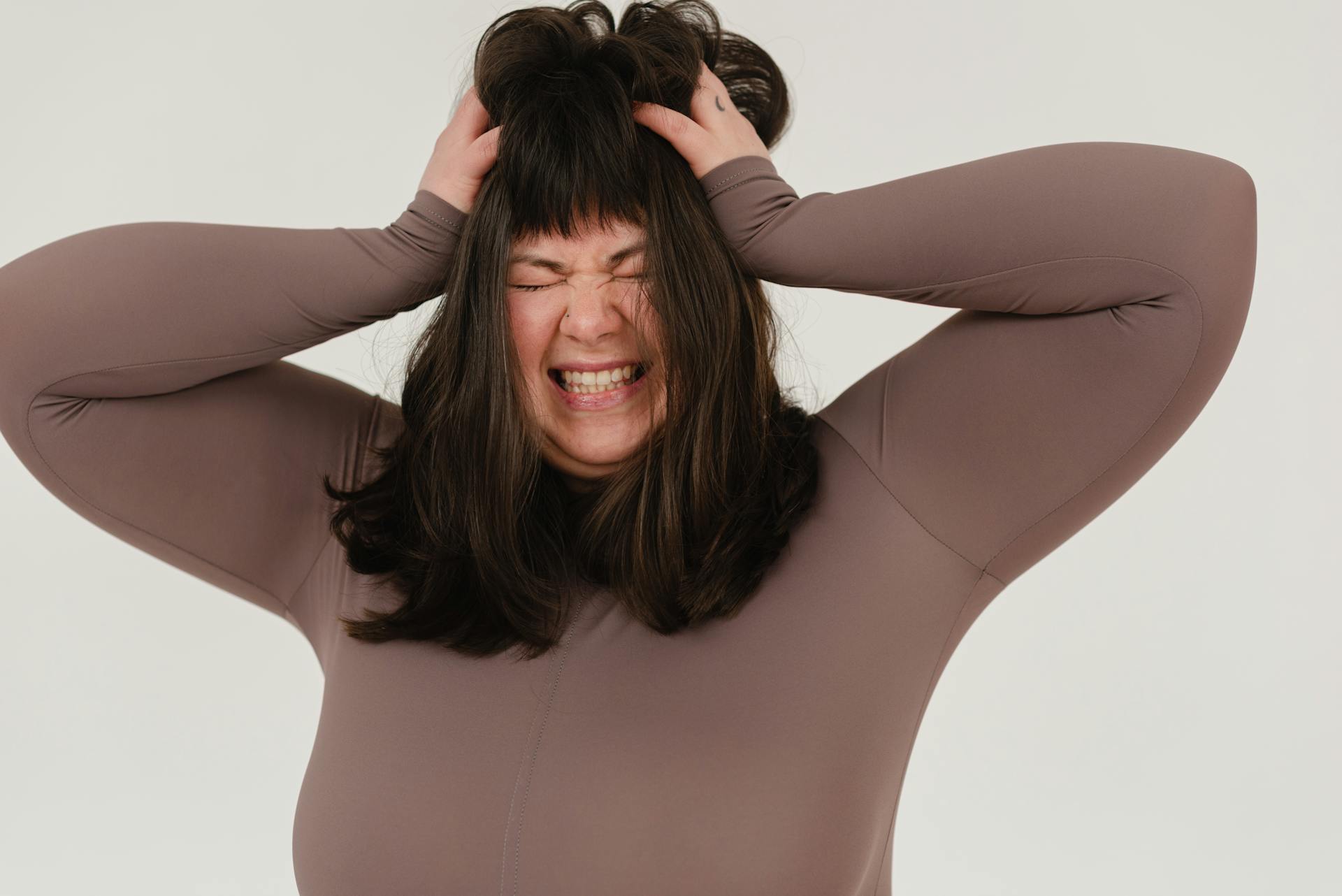 Young obese woman rumpling hair with closed eyes in white studio