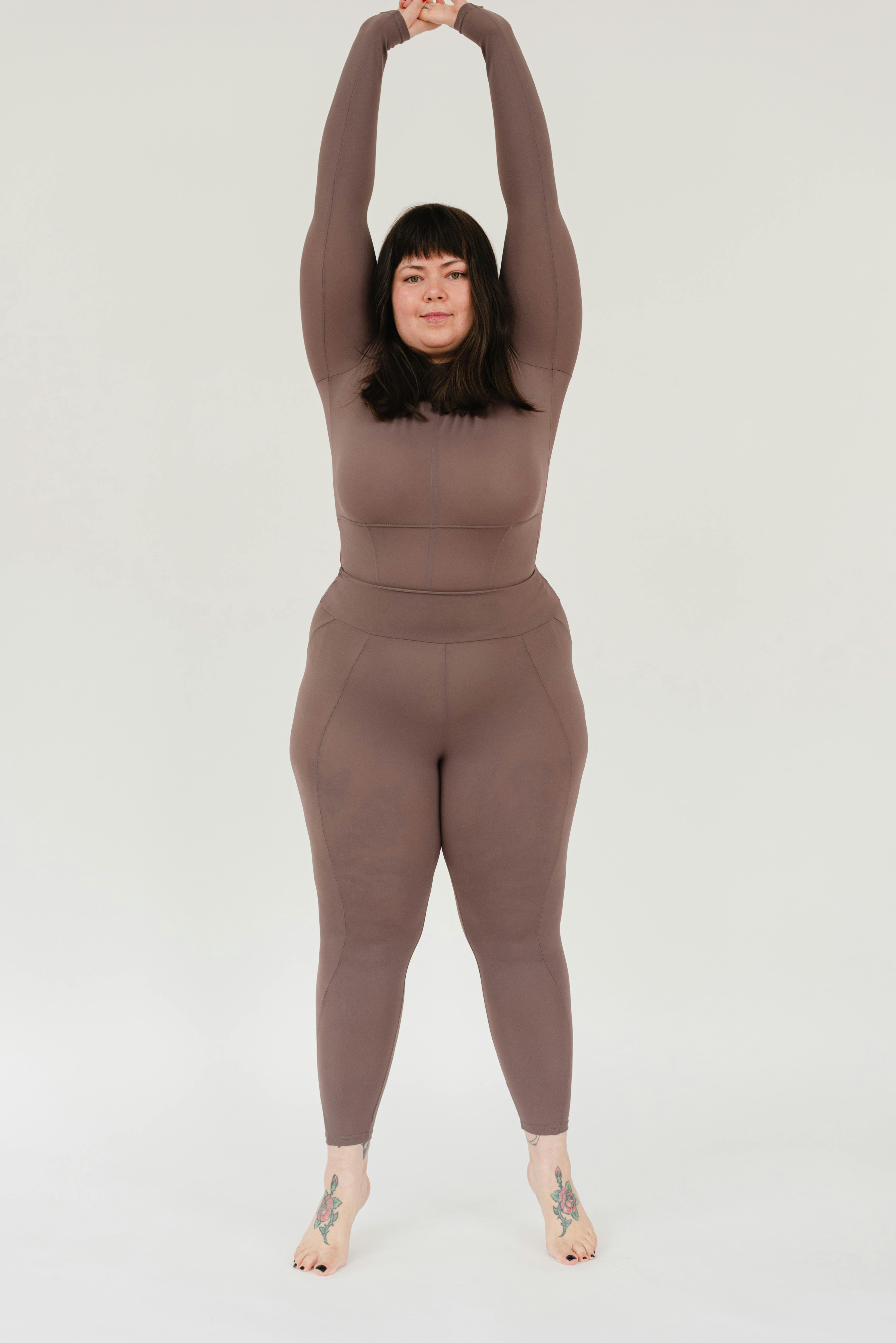 plus size woman stretching arms and looking at camera in white studio