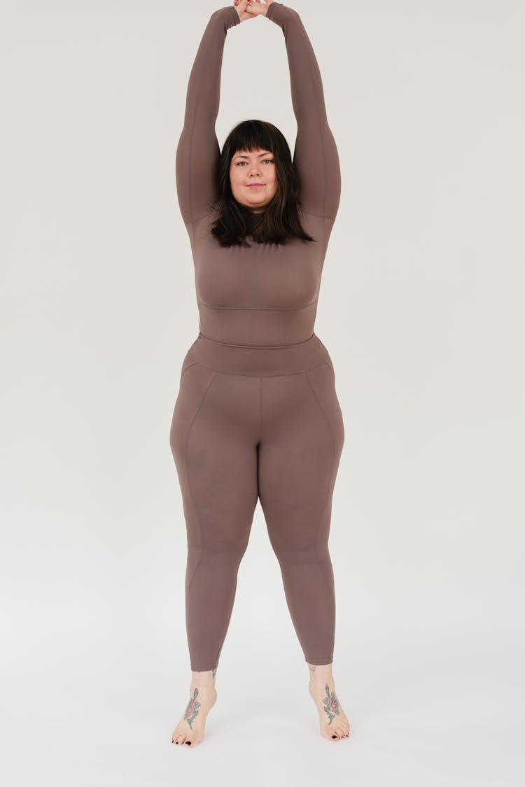 Plus Size Woman Stretching Arms And Looking At Camera In White Studio