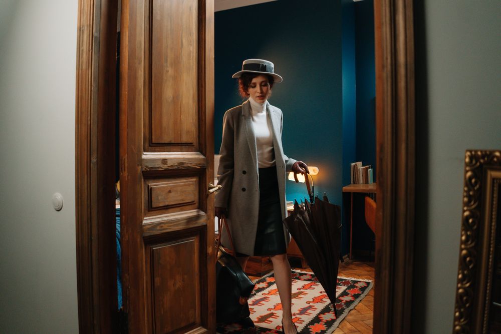 Woman in a grey coat and hat stepping through a tall panelled doorway — photo by cottonbro studio on Pexels