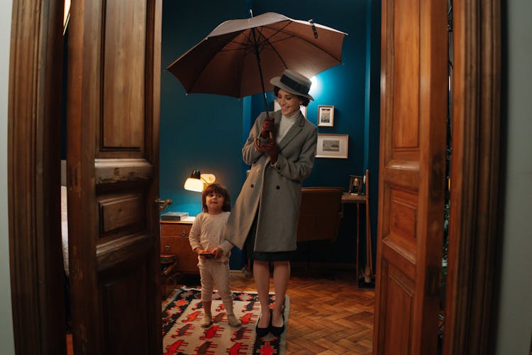 A Woman Holding An Umbrella Beside A Child