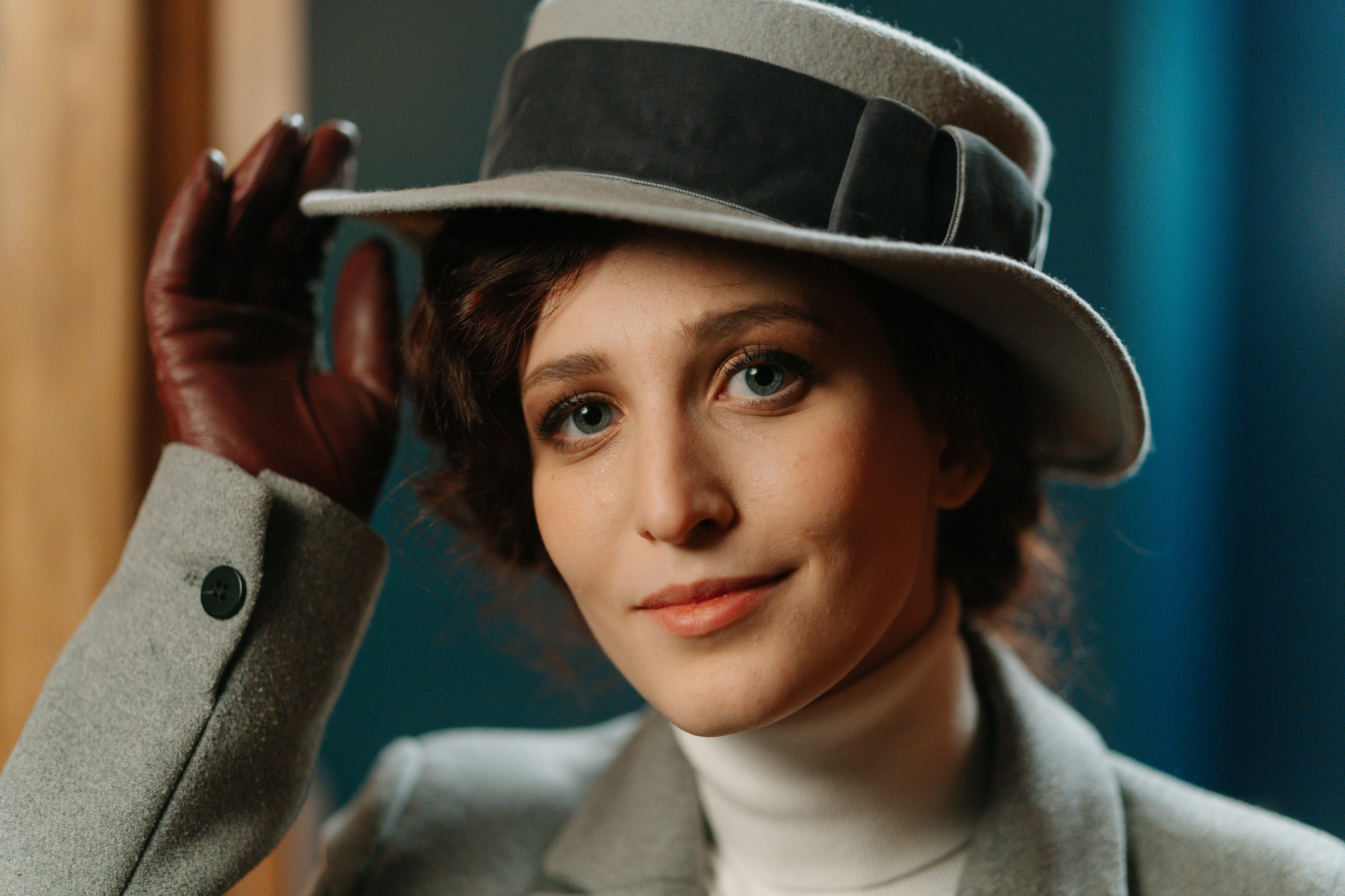 Portrait of a young woman wearing a stylish vintage hat and gloves indoors.