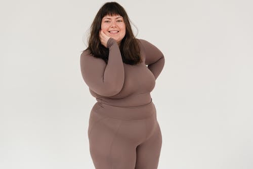 Positive plus size female wearing tight sportswear standing with hand on cheek against white background