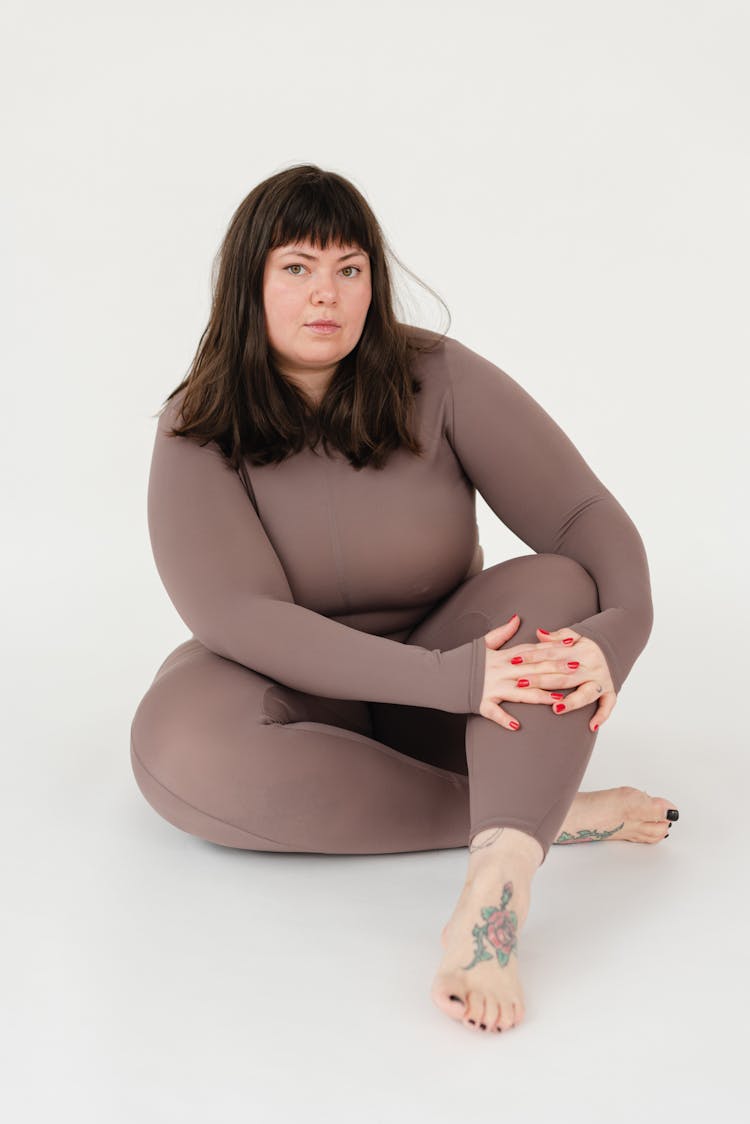 Plump Female In Activewear Sitting With Crossed Legs In Studio