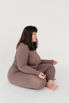 A plus size woman practicing meditation in a tranquil studio setting on a white background.