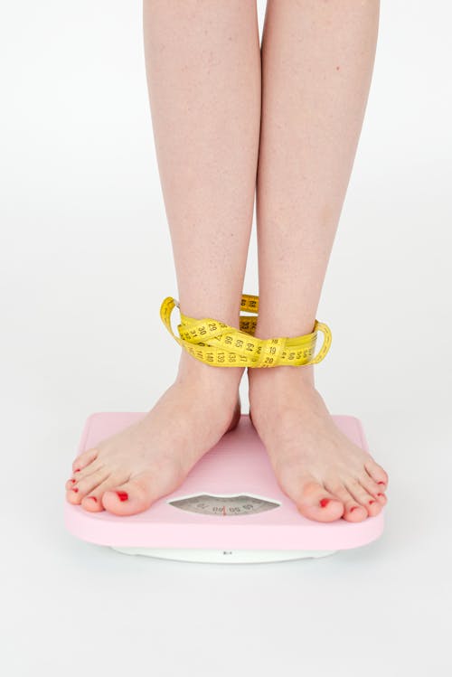 Free High angle of crop anonymous female with centimeter on legs checking weight on scales on white background Stock Photo