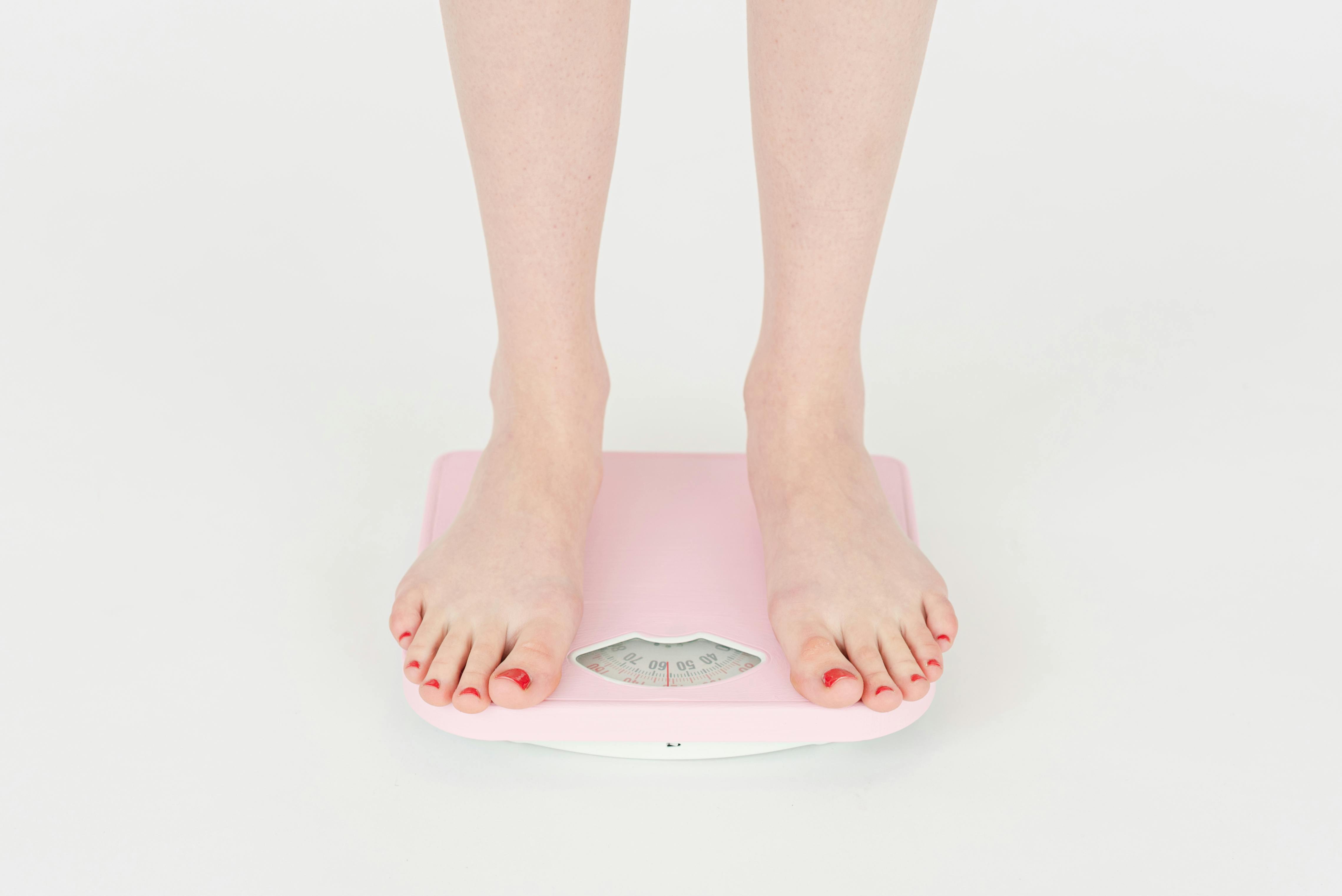 Woman feet and pink weight scale isolated on white background