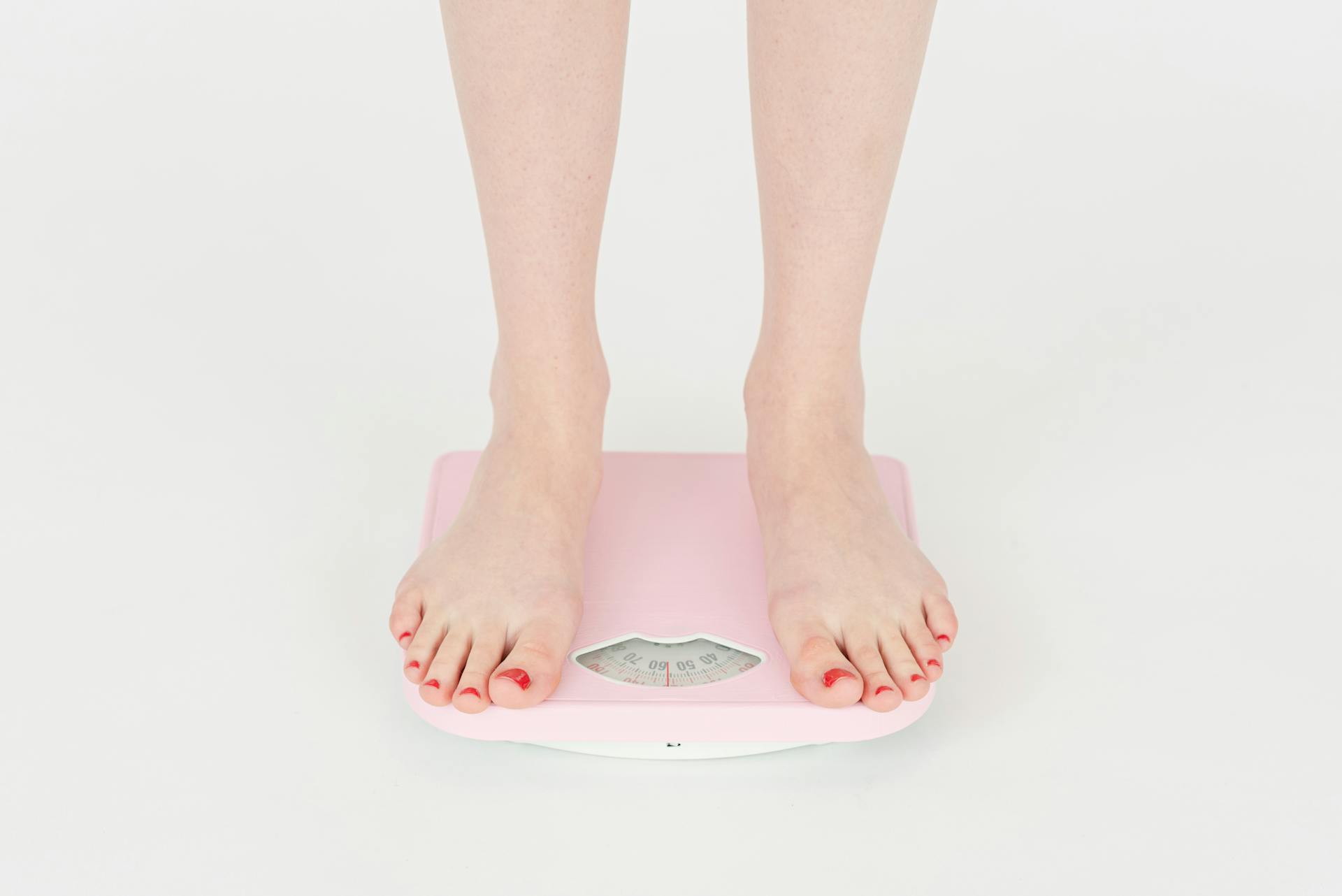 High angle of crop anonymous female measuring weight for control body against white background in studio