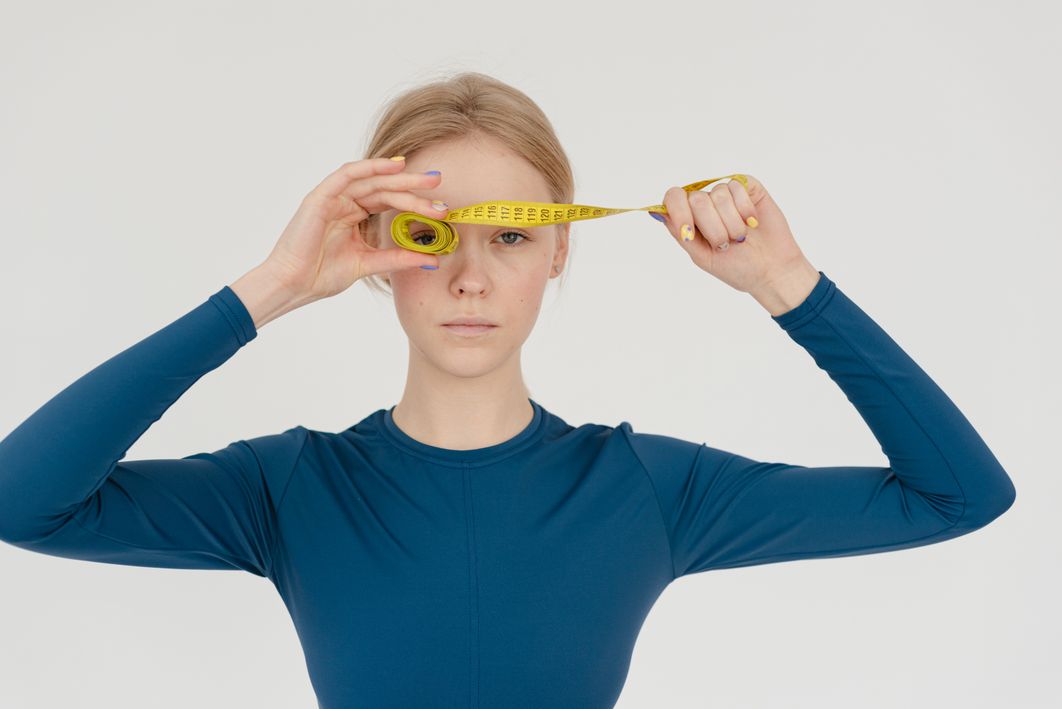 Ozempic Face: Causes and How to Prevent Sagging Skin During Weight Loss 1 Serious woman holding a rolled measuring tape in a studio setting