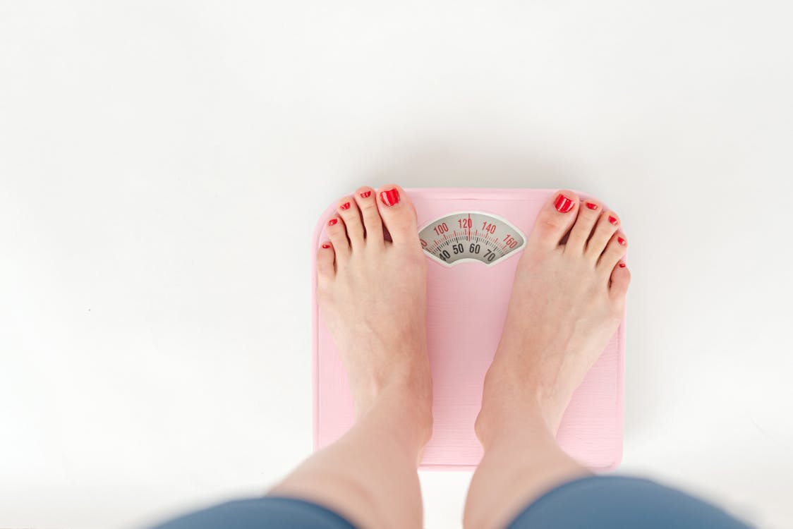 Top view of crop anonymous barefoot female measuring weight on scales on white background