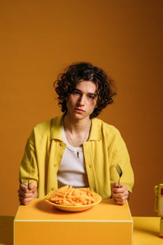 Young man with curly hair eating fries, set against a vibrant retro orange background.