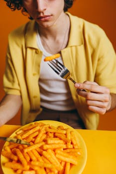 Young man in yellow attire enjoys a crispy potato snack against a vivid orange background.