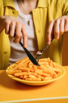 A young man enjoying a plate of crispy snacks with a knife and fork against a yellow background.