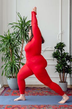 Woman in red activewear performing yoga Warrior Pose indoors on a colorful rug.