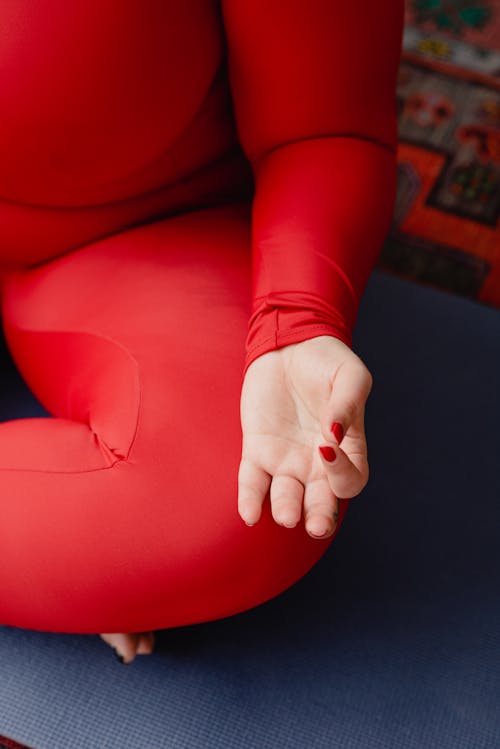 Free Unrecognizable plus size female in red sportswear sitting in lotus pose while doing yoga exercise on mat during workout in room Stock Photo