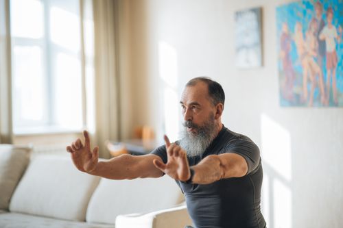 Free A senior man stretches in a bright living room, embracing fitness and positive aging. Stock Photo