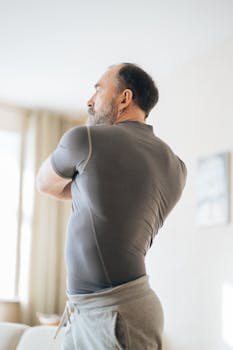 Elderly man in activewear stretching indoors for healthy living and fitness.