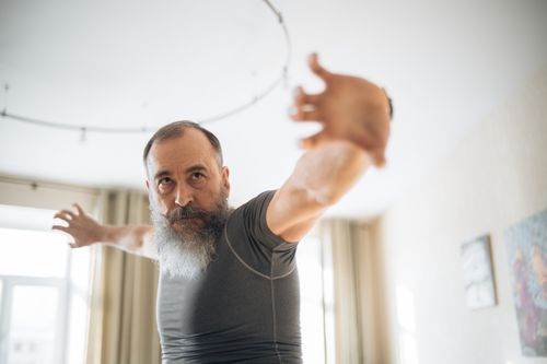 Free Elderly man with beard doing yoga stretches in a room, enhancing fitness and relaxation. Stock Photo