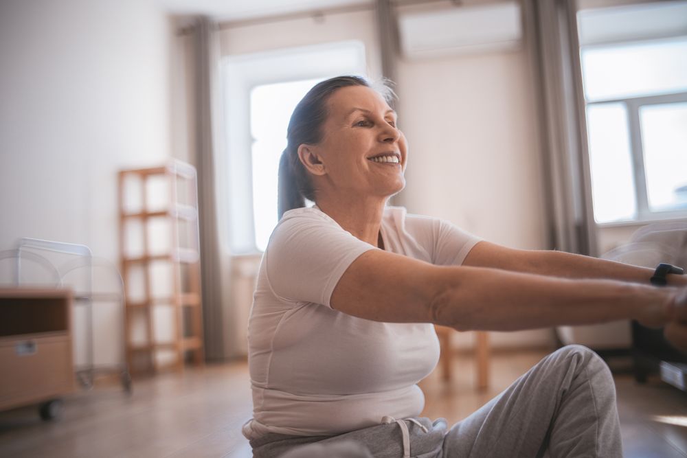 A smiling woman in her 50s exercising in the warm light of her living room