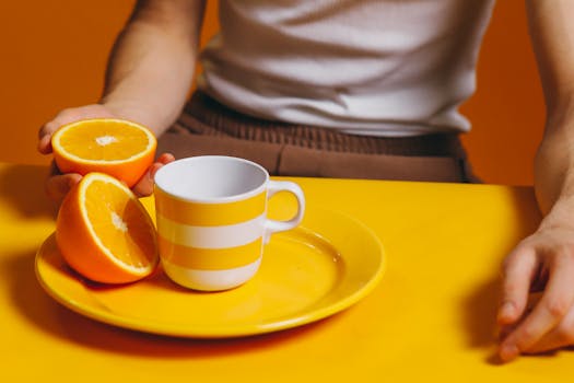 A dynamic orange-themed setup with fresh oranges and a striped mug on a bright yellow plate, perfect for healthy lifestyle content.