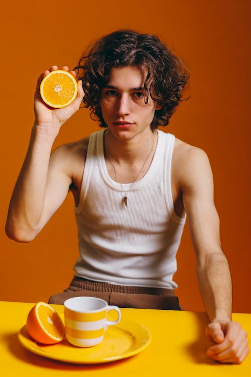 Young Man Holding Up A Slice Of Orange Fruit 