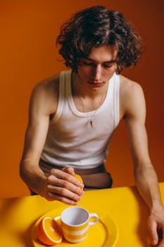 Young man squeezing orange juice into a cup on a vibrant background.