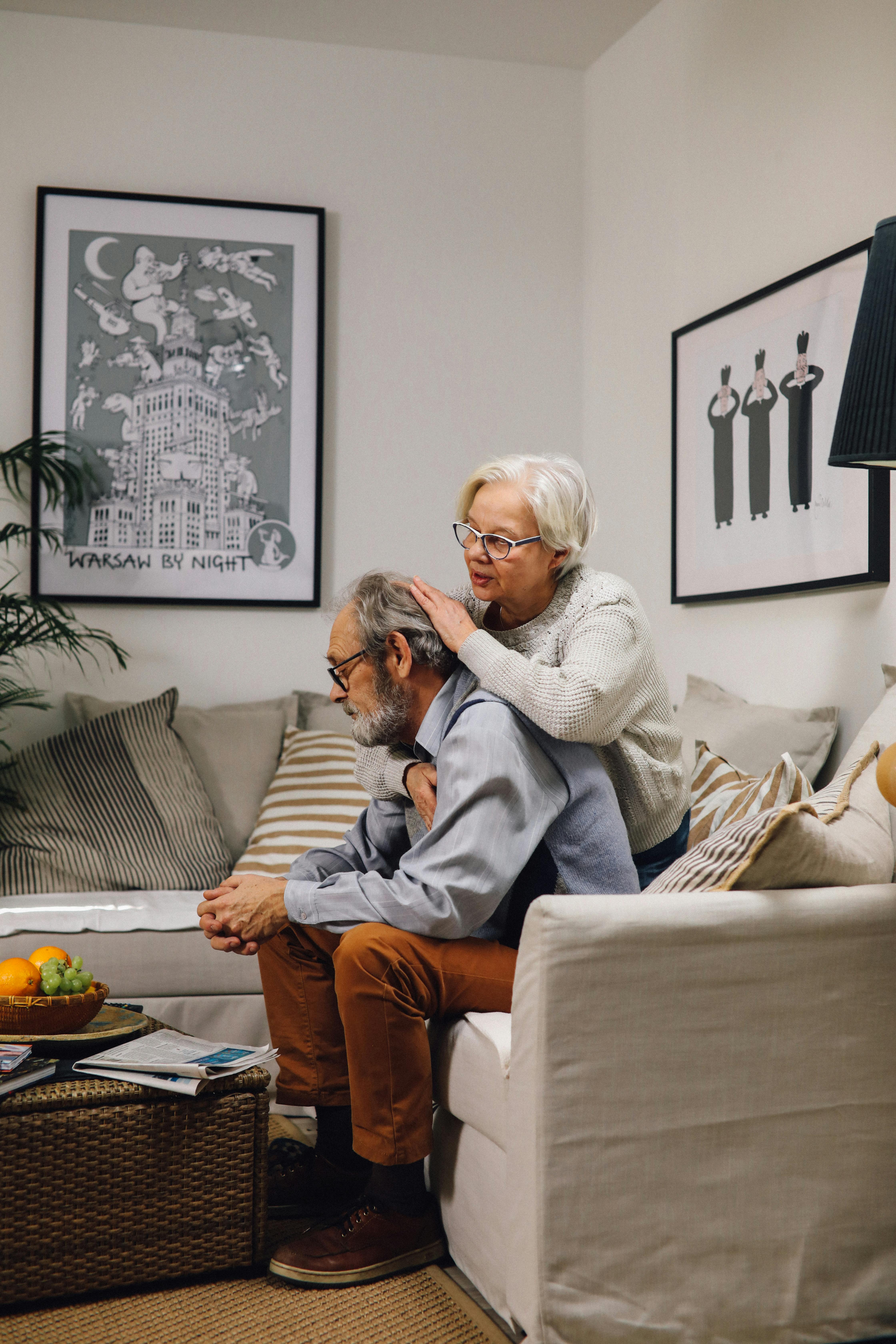 A senior couple shares a warm embrace on the sofa in their living room, exuding affection and comfort.