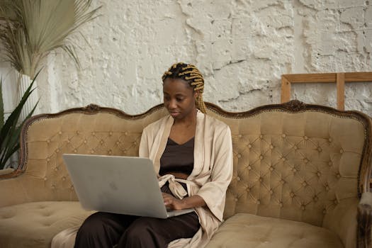 An African American woman working remotely on her laptop, seated on a vintage sofa at home.
