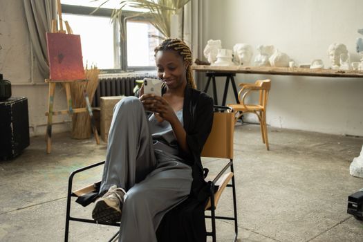 Woman sitting comfortably in art studio, engaging with her mobile phone.
