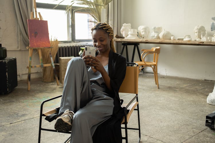 A Smiling Woman Sitting On The Chair While Using Her Phone