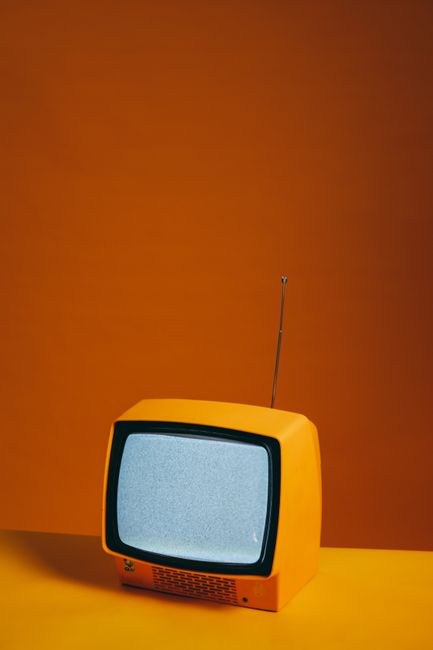 Vintage yellow TV set with antenna against a vibrant orange backdrop creating a retro feel.