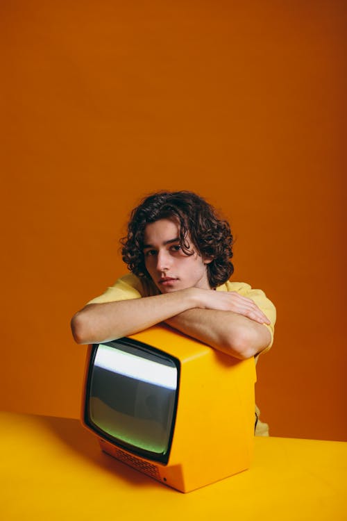 Young Man Sitting Beside A Yellow Television