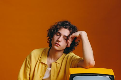 Free Young man with curly hair in vibrant yellow attire resting on a vintage TV set. Stock Photo