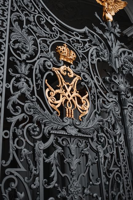 Close-up of an intricate iron gate with a golden royal emblem in St. Petersburg, Russia.