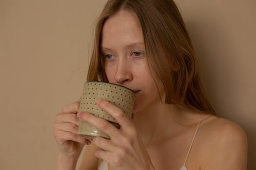 A calm woman enjoys a warm beverage, captured in a minimalist studio setting.
