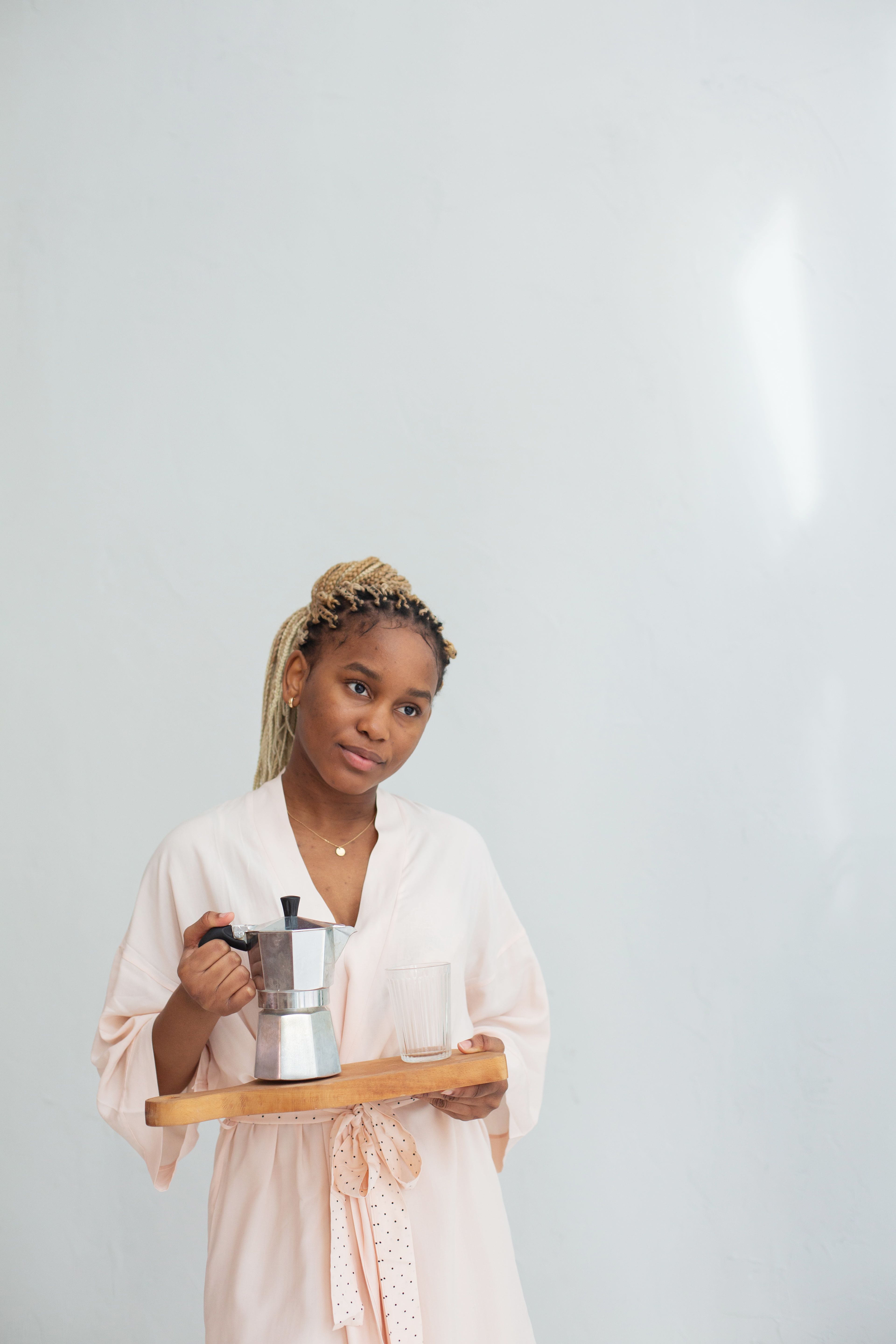 Portrait of a young woman holding a coffee kettle on a tray, set against a plain background.
